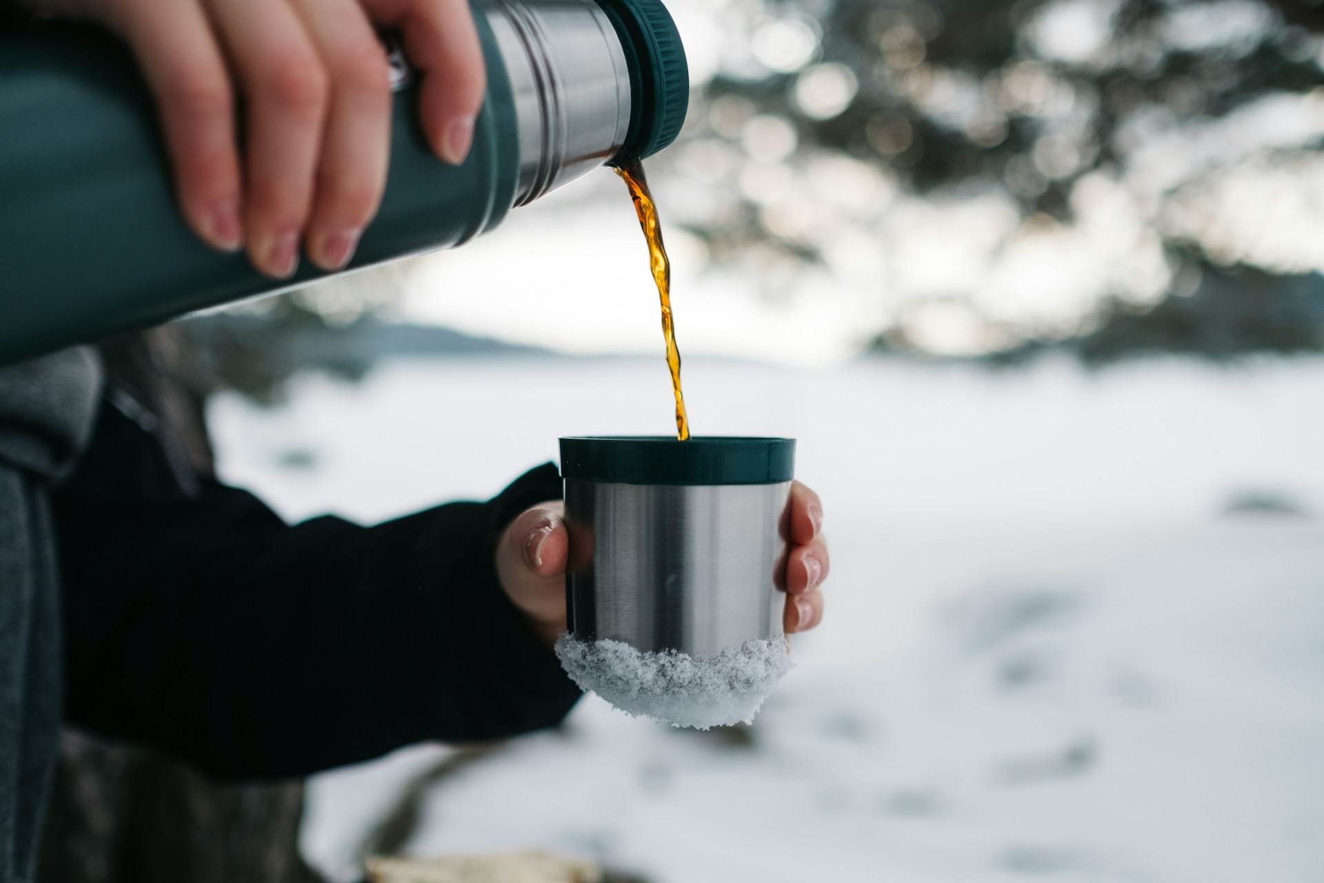 Closeup of a person pouring hot coffee from a thermos while outside in the snow.