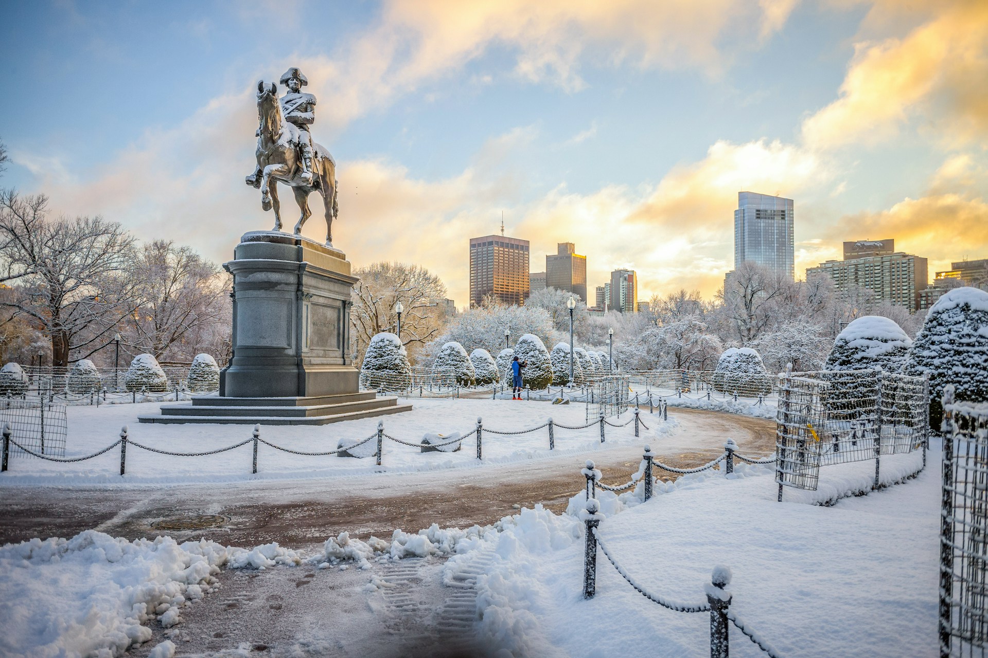 Old statue of a man riding a horse in a snow-covered park in Boston park.